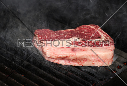 Close up searing and smoking ribeye beef steaks on open outdoor grill with cast iron metal grate, high angle view