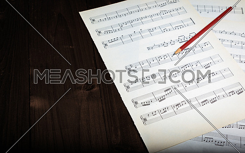 In the picture aged pages of sheet music, pencil  and wooden background.