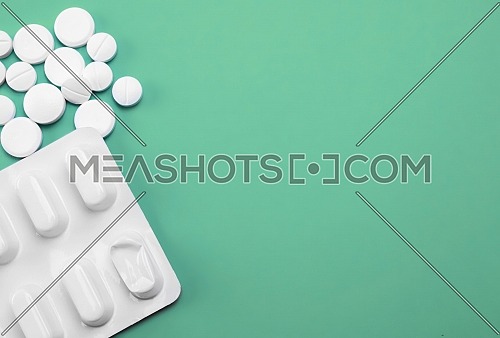 Blister and white tablets isolated on green background, conceptual image