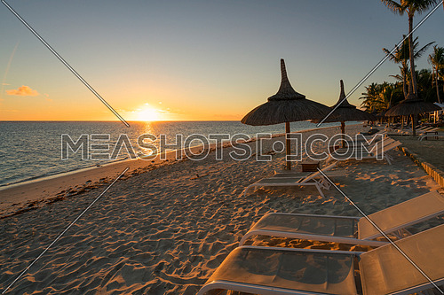 Amazing sunset, sandy beach with deckchairs and parasols typical of the Mauritius resorts
