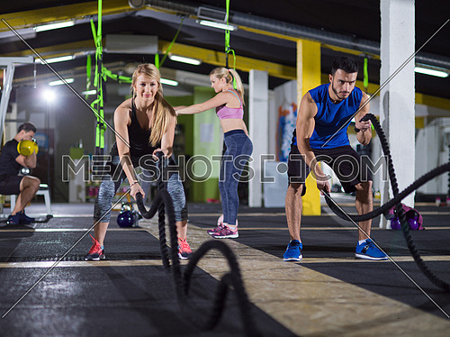 young fit sports couple working out in functional training gym doing crossfitness exercise with battle ropes