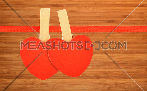 Valentine day template, two red wooden hearts with clothes pins on textile ribbon over bamboo wood board surface