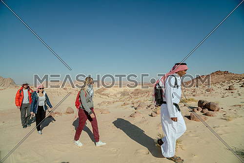 Group of tourists walking on sands with bedouin guide while exploring Sinai Trail in Ain Hodouda by day.