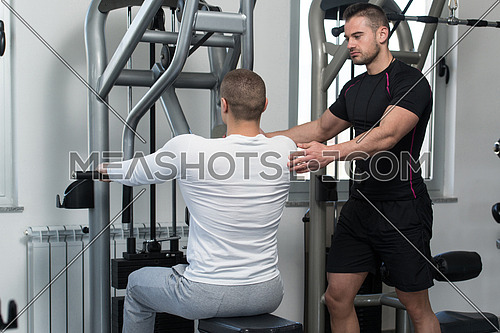 Personal Trainer Showing Young Man How To Train Back On Machine In The Gym