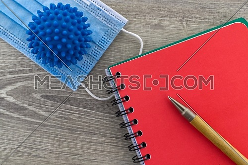 Symptoms of coronavirus and medical concept with a surgical face mask with a corona virus model alongside a wire bound notepad and pen