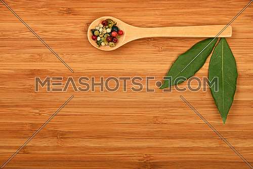 Two bay laurel leaves and mix of peppercorn in wooden spoon on bamboo wood chopping board background