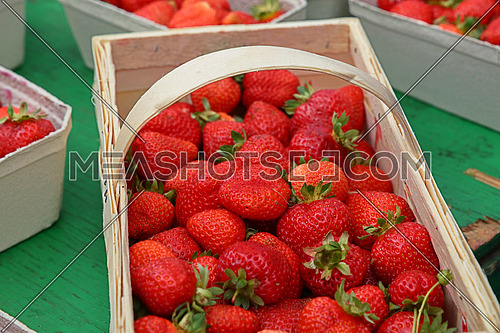 Close up red ripe fresh strawberry with green leaves in big wooden basket crate on retail display of farmers market stall, high angle view