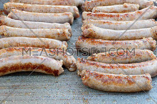 Pictured pork sausages placed in two vertical rows are cooked on the grill.
