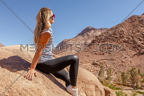 long shot for a female tourist stiing on a rock explore Sinai Mountain for wadi Freij at day.
