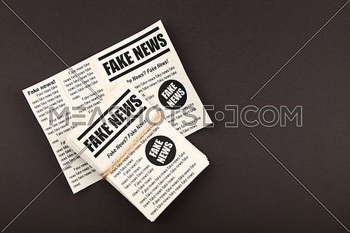 Close up stack of FAKE NEWS newspapers over black paper background with copy space, elevated top view, directly above