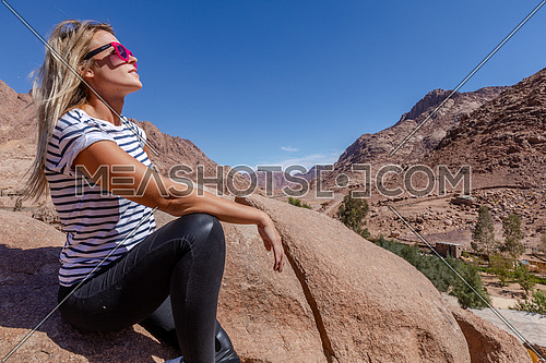 long shot for a female tourist stiing on a rock explore Sinai Mountain for wadi Freij at day.