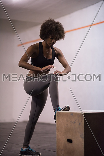 Fit young african american woman are preparing for box jumping at a crossfit style gym. Female athlete is performing box jumps at gym.