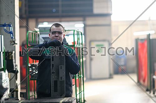 a uniformed worker working in a modern metal production and processing factory assembles parts of a new machine on his desk. High quality photo