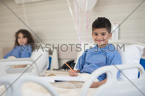 little middle eastern boyl painting home and family at hospita bed in a large modern hospital