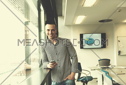 relaxed young businessman using smart phone at modern startup business office meeting room  with big window and city in backgronud