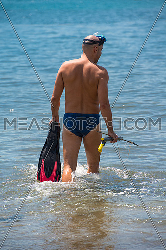 Young smiling fisherman with equipment standing in the shallow water of the sea while preparing for underwater fishing  active holiday concept