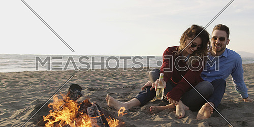 Young Couple Relaxing By The Fire, Drinking A Beer Or A Drink From The Bottle.