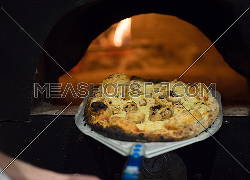 chef using special shovel to removing hot pizza from  stove where it was baked