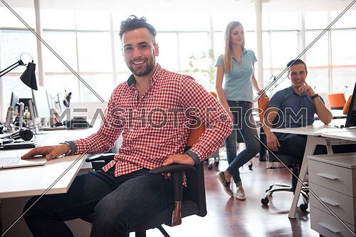 Portrait of smiling young informal businessman with colleagues in background at the office