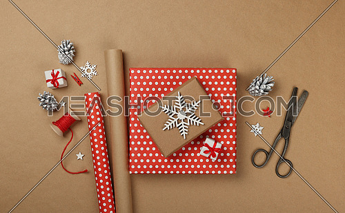 Close up flat lay of packing and wrapping Christmas gift boxes with red paper, table top view, directly above
