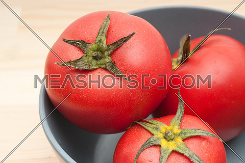 fresh ripe tomatoes on a blue bowl over pine wood table