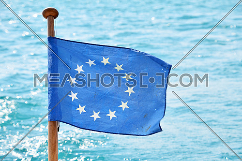 Close up flag of EU, European Union waving and blowing in the wind over blue water of sea or lake, low angle view