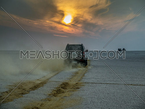 An SUV driving in the desert during sunset towards the horizon