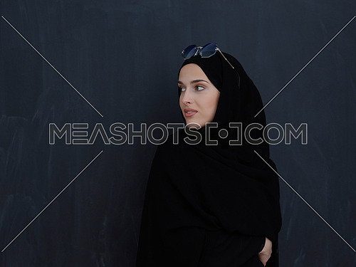 Young muslim in traditional clothes or abaya and sunglasses posing in front of black chalkboard. Arab woman representing modern arabic lifestyle, islamic  fashion and Ramadan kareem concept