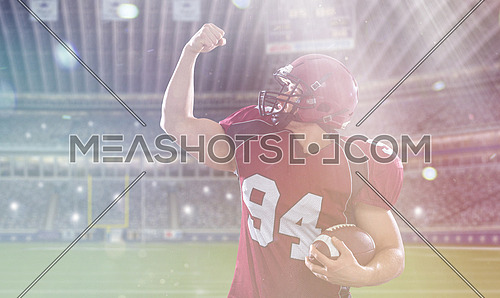 american football player celebrating touchdown on big modern stadium field with lights and flares
