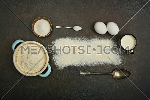 Close up flat lay of baking ingredients on dark grunge stone table surface with copy space, milk, flour, eggs, salt, sugar, pannikin and utensils, elevated top view, directly above