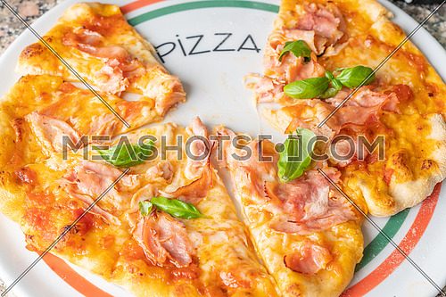 Fresh italian pizza with cheese(mozzarella), tomato, ham and small fresh basil leaves on the plate the inscription Pizza.