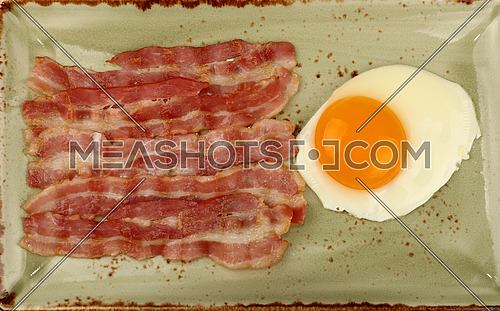 Close up English breakfast, sunny side egg and roasted bacon slices on blue plate, elevated top view, directly above