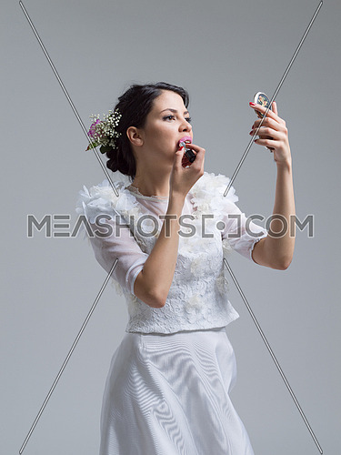 bride paints lips with lipstick on their wedding day in dress isolated on a white background