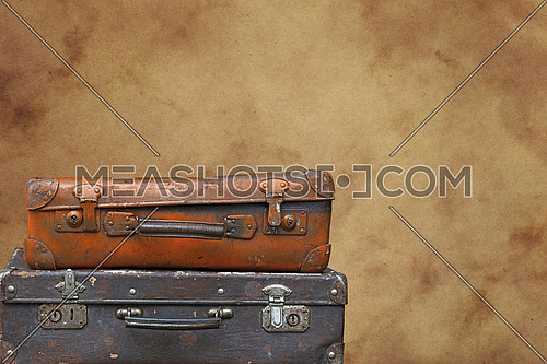 Close up stack of two old vintage antique grunge travel luggage brown leather suitcase trunks isolated over background of brown paper parchment, low angle side view