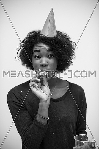 portrait of a young beautiful black woman in party hat blowing in whistle isolated on a white background