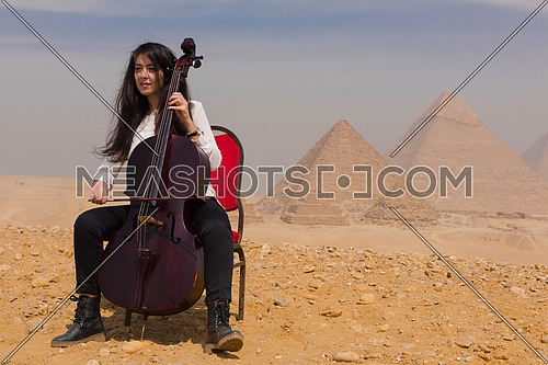 young famale chello player in egyptian desert with pyramids in background