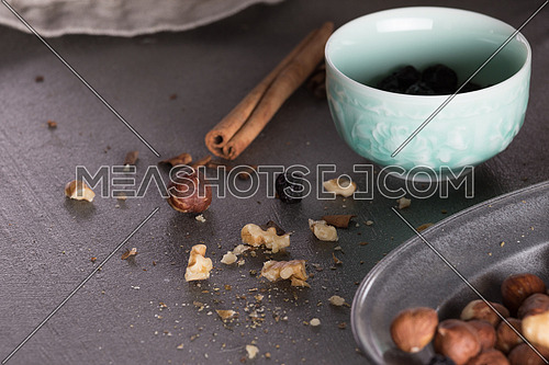 Dry nuts in a metal tray and a blue bowl with raisins and cinnamon sticks