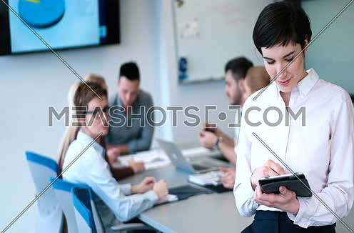 Portrait of smiling casual businesswoman using tablet with coworkers sitting in background