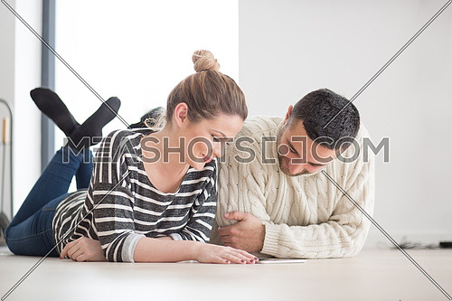 Young Couple on the floor in front of fireplace surfing internet using digital tablet on cold winter day