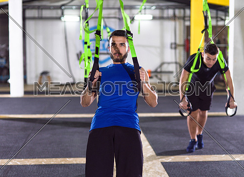 two young athlete men working out pull ups with gymnastic rings at the crossfitness gym
