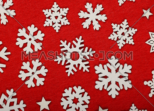 Close up pattern of white wooden snowflakes Christmas decoration over red felt background, table top view, flat lay