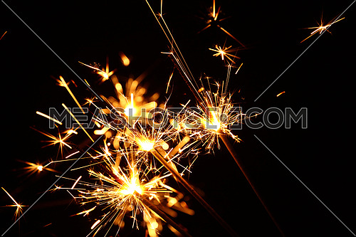 Close up group of several festive firework sparklers over black background, low angle side view, selective focus