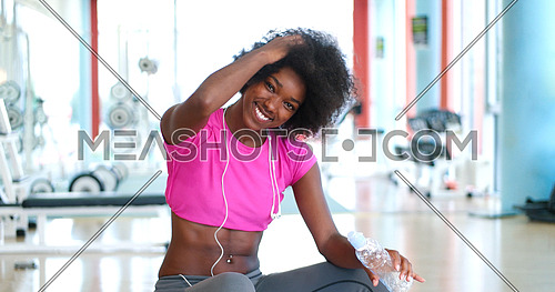 portrait of young afro american woman in gym on workout break while listening music on earphone