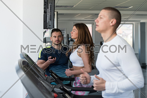 Group Of Young People Running On Treadmills In Gym Or Fitness Club While Personal Trainer Measure Time On Stopwatch