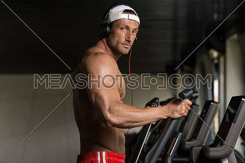 Muscular Mature Man Doing Aerobics Elliptical Walker In Modern Fitness Center