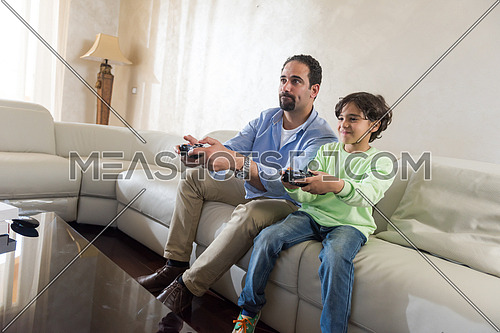 Middle Eastern father and son playing video games and cheerfully spend time on the sofa