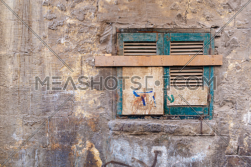 Old grunge window with closed green broken shutters on dirty cracked bricks stone wall