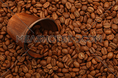 Close up fresh roasted Arabica coffee beans poured out of brown ceramic cup, high angle view