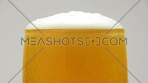 Close up background of pouring beer with bubbles and foam in glass, overfill and run out, flowing over the top, low angle side view, slow motion