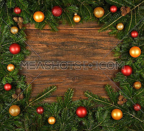 Close up border frame of fresh green spruce or pine Christmas tree branches with cones and colorful balls and baubles decoration, over dark brown wooden planks background with copy space